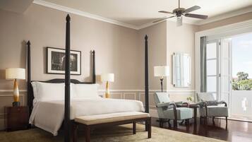 A four-poster bed with a canopy, two bedside lamps, a ceiling fan, and a view of the outdoors through a large window.