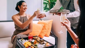 Een kamer met een bank, een dienblad met eten en drinken, en een persoon die iets te drinken inschenkt.