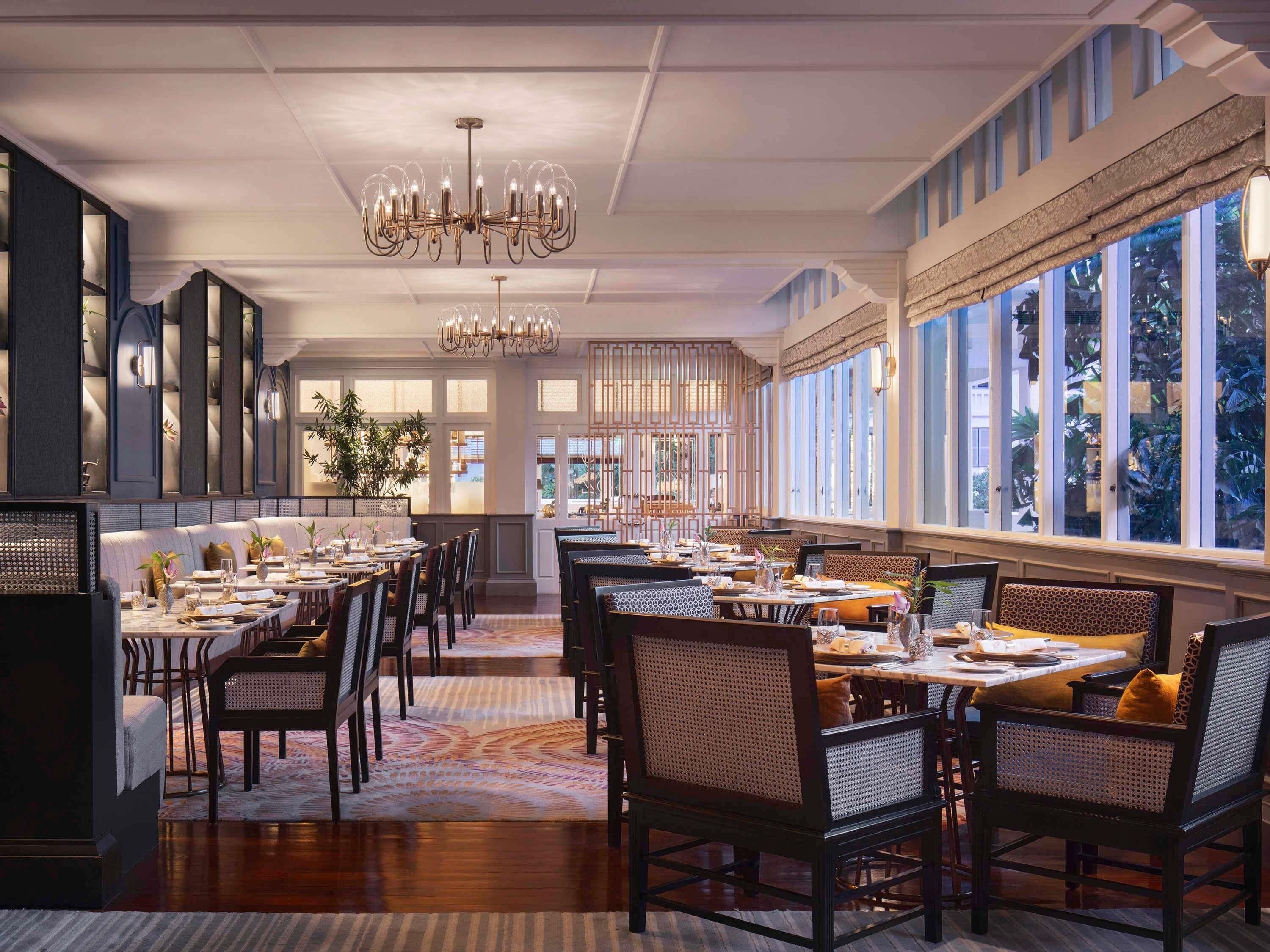 A spacious dining area with high ceilings, chandeliers, and large windows offering views of the outdoors.