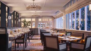 A spacious dining area with high ceilings, chandeliers, and large windows offering views of the outdoors.