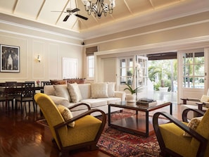 Amplia sala de estar con techo alto, un candelabro, un comedor con mesa y sillas, y ventanas grandes con vistas al exterior.
