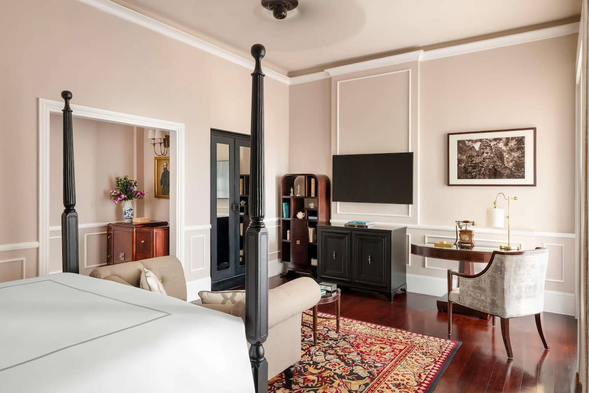 A bedroom with a four-poster bed, a television, a bookshelf, and a desk with a lamp.