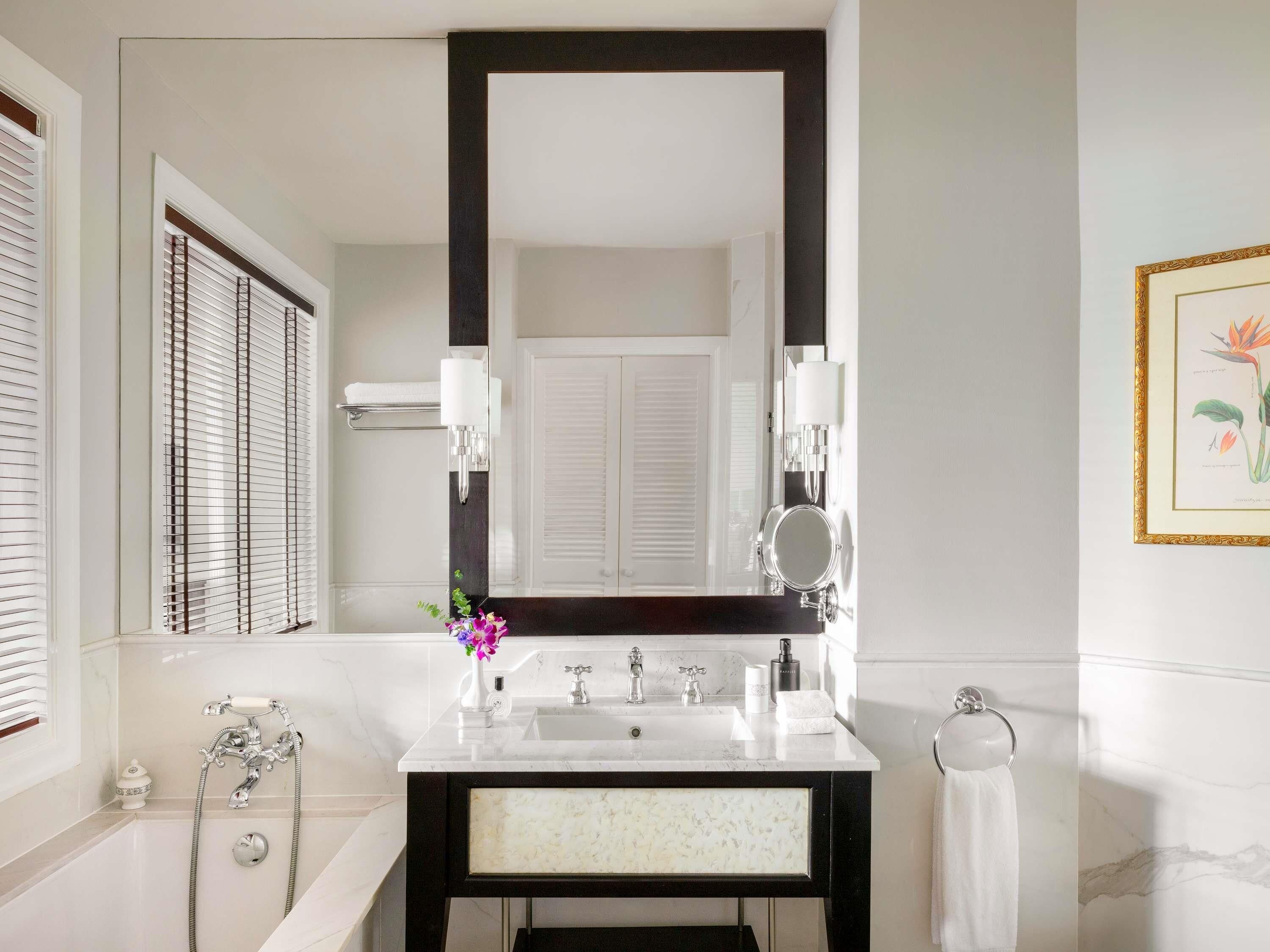 Un baño con un espejo grande, lavamanos blanco y una bañera.