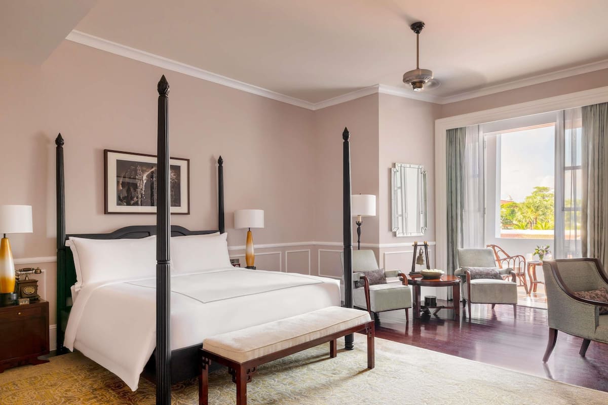 A four-poster bed with a bench, a chair, a table, and a view of the outdoors.