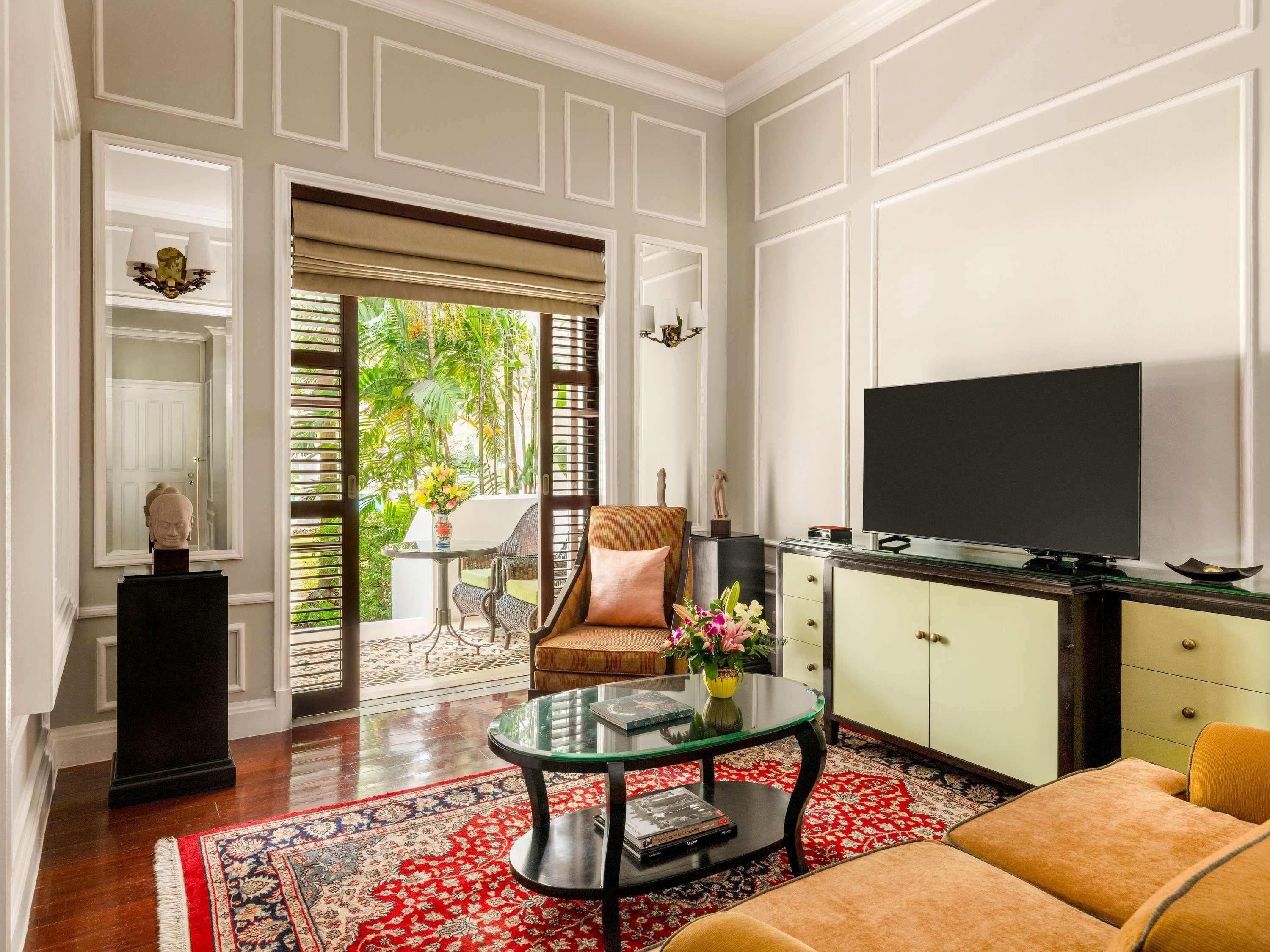 A spacious living room with a large TV, comfortable seating, a glass coffee table, and a view of the outdoors.
