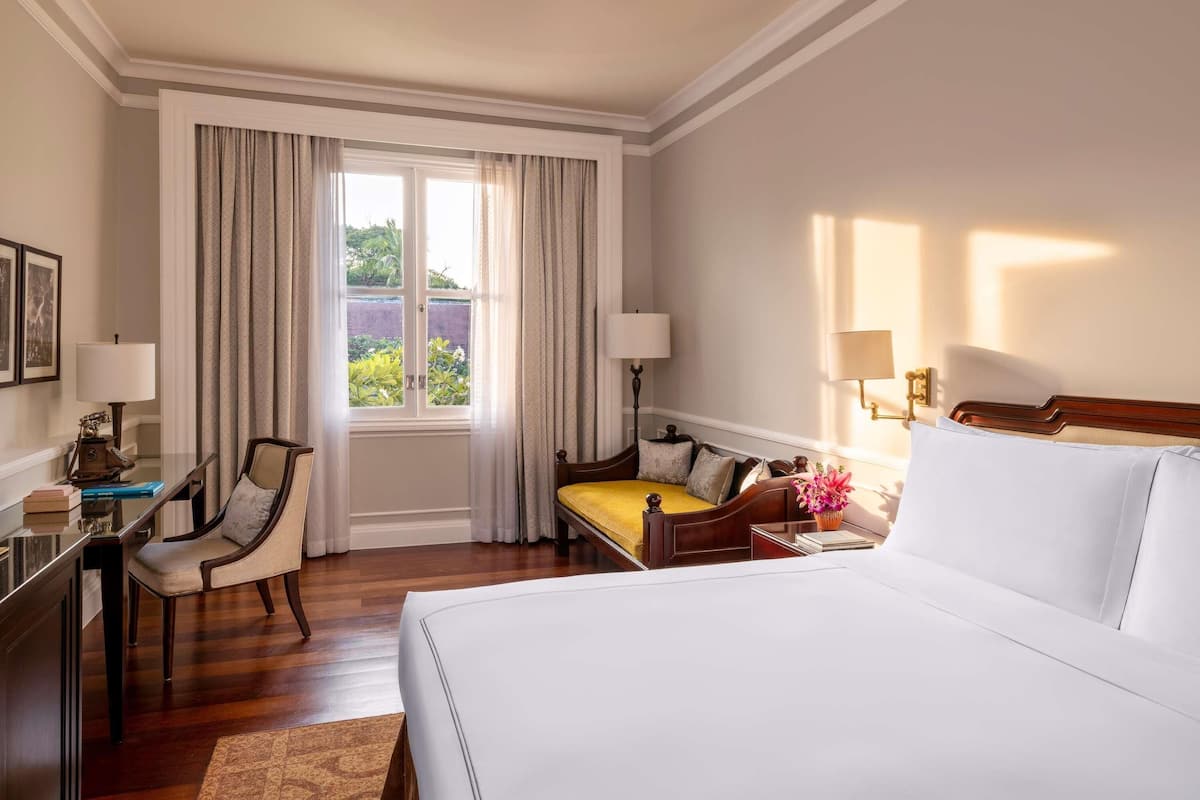 A hotel room with a large bed, a desk with a lamp, a chair, and a window with curtains.