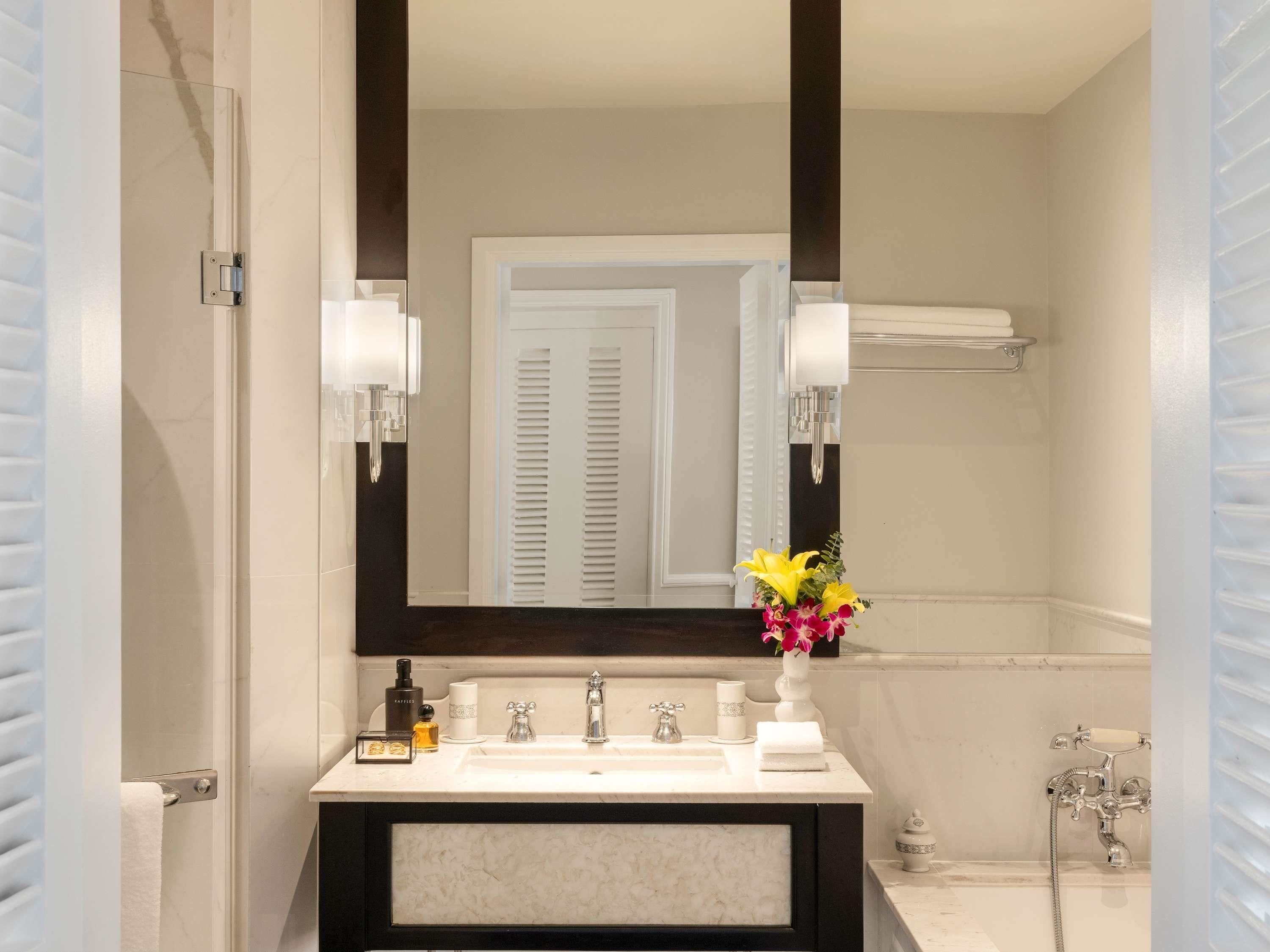 Une salle de bain avec un grand miroir, un lavabo à deux robinets, un porte-serviettes et une douche.