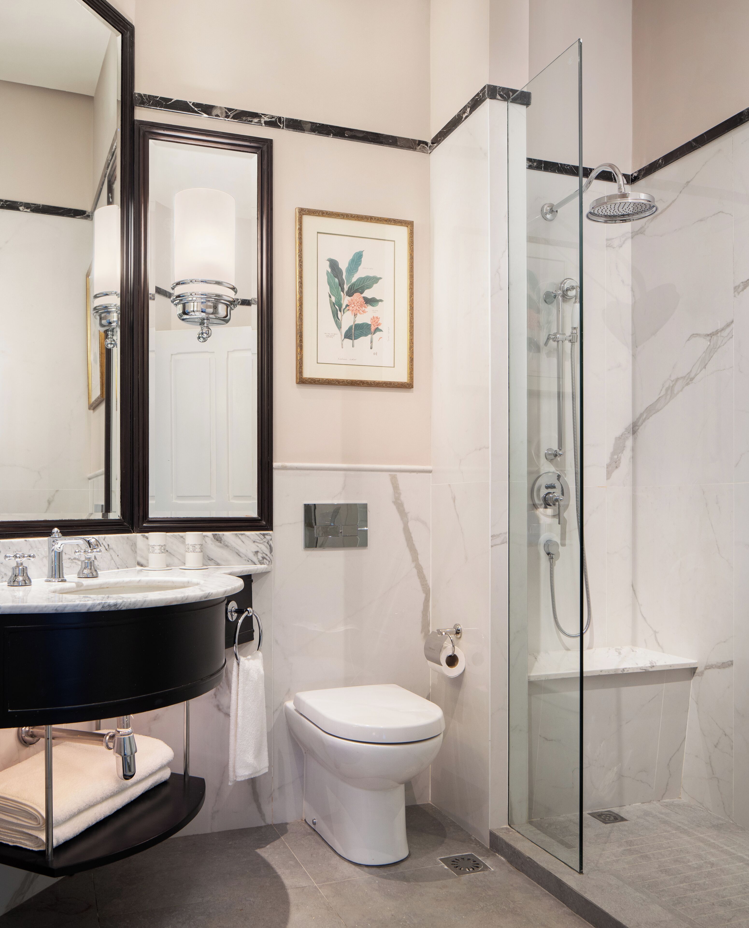 A modern bathroom with a marble sink, a toilet, a shower with a glass door, and a framed botanical print on the wall.