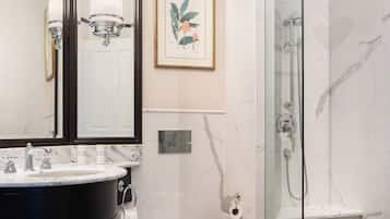 A modern bathroom with a marble sink, a toilet, a shower with a glass door, and a framed botanical print on the wall.