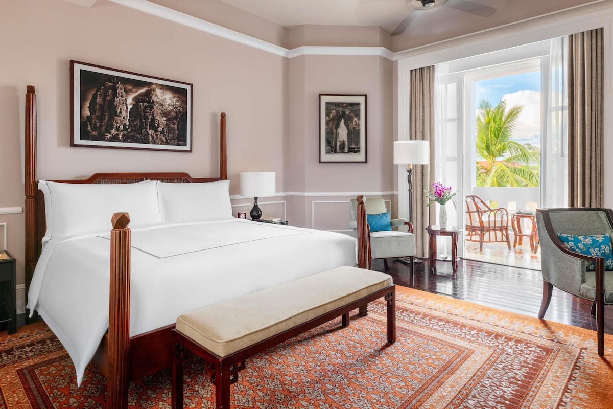 A hotel room with a large bed, a bench, a desk, a chair, and a view of palm trees.
