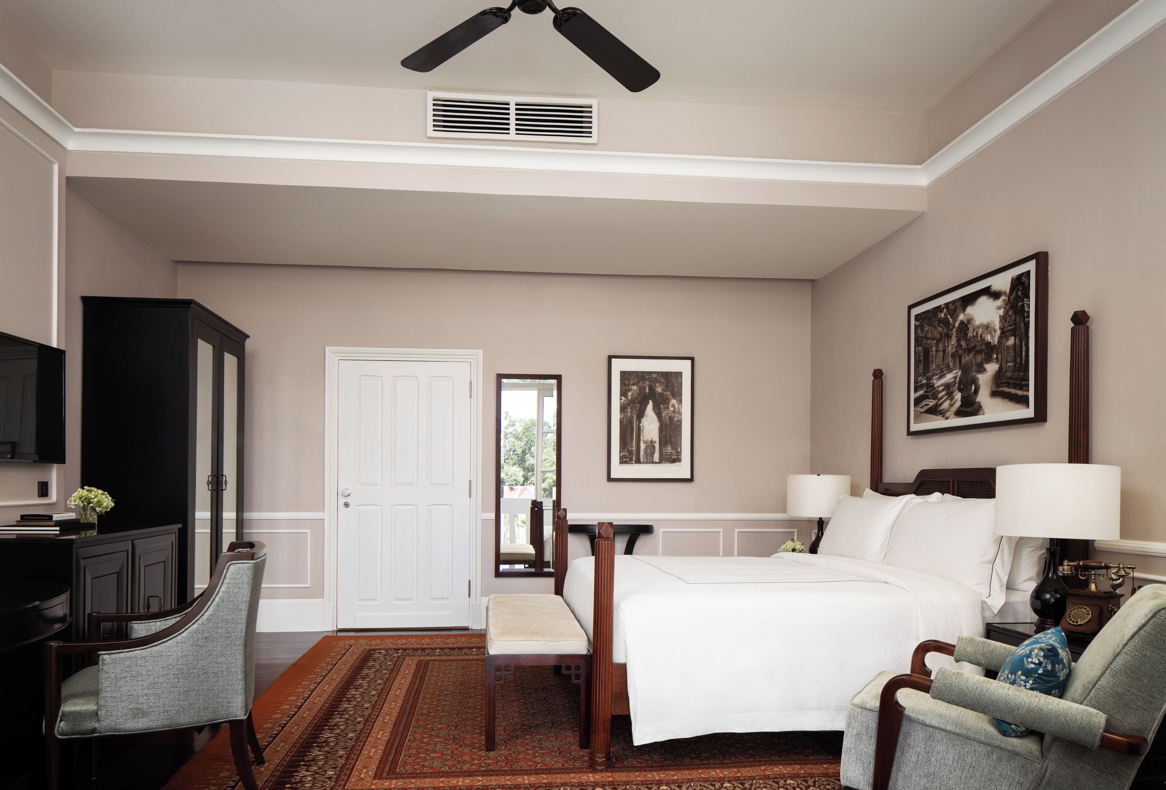 A hotel room with a bed, a desk, a chair, a television, and a ceiling fan.