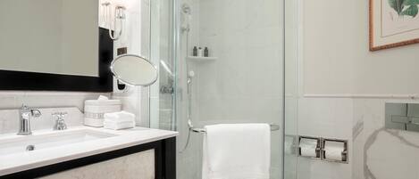A modern bathroom with a glass-enclosed shower, a white sink with a marble countertop, and a framed botanical print on the wall.