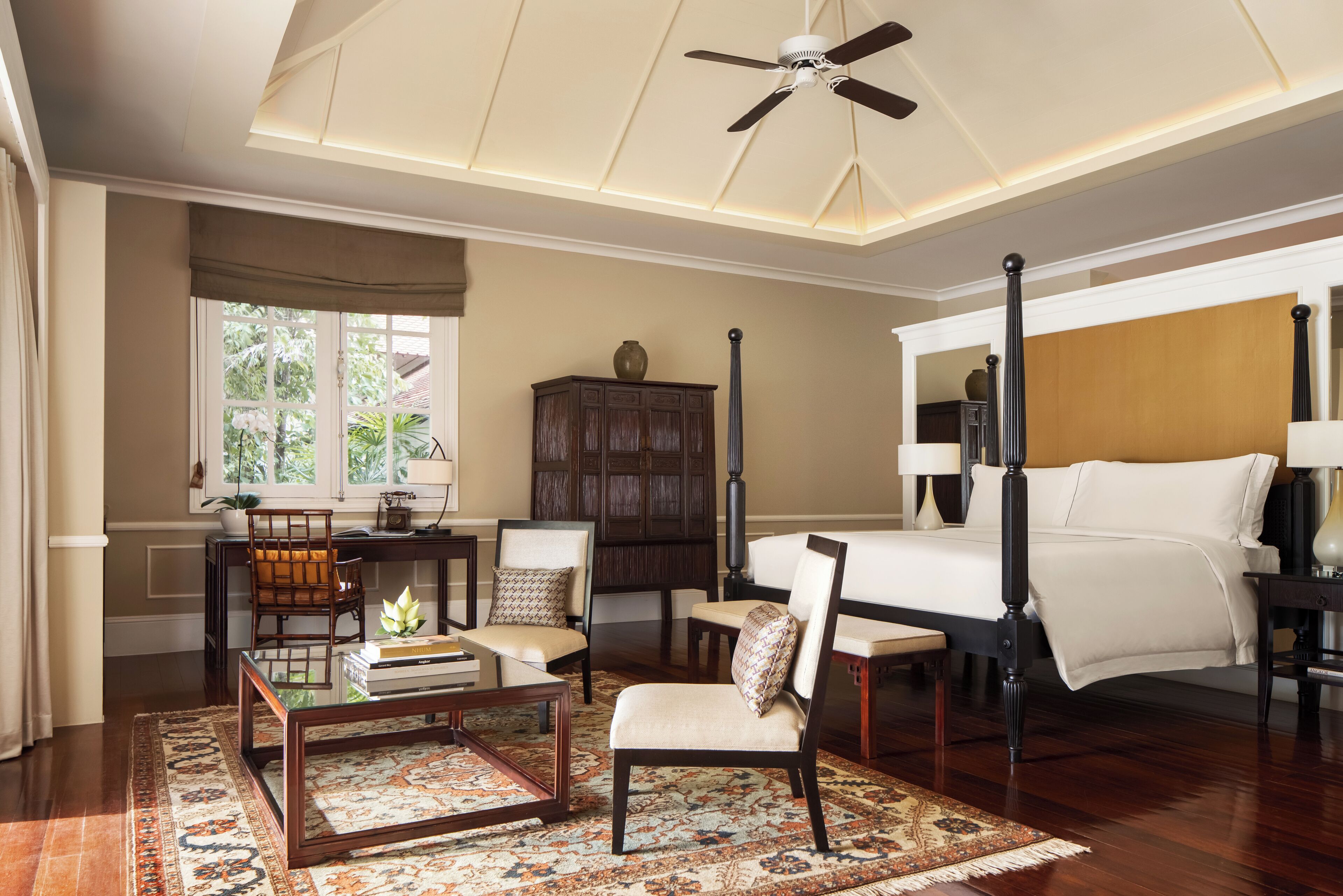 A spacious room with a large bed, a ceiling fan, a wooden cabinet, and a window with a view of greenery.