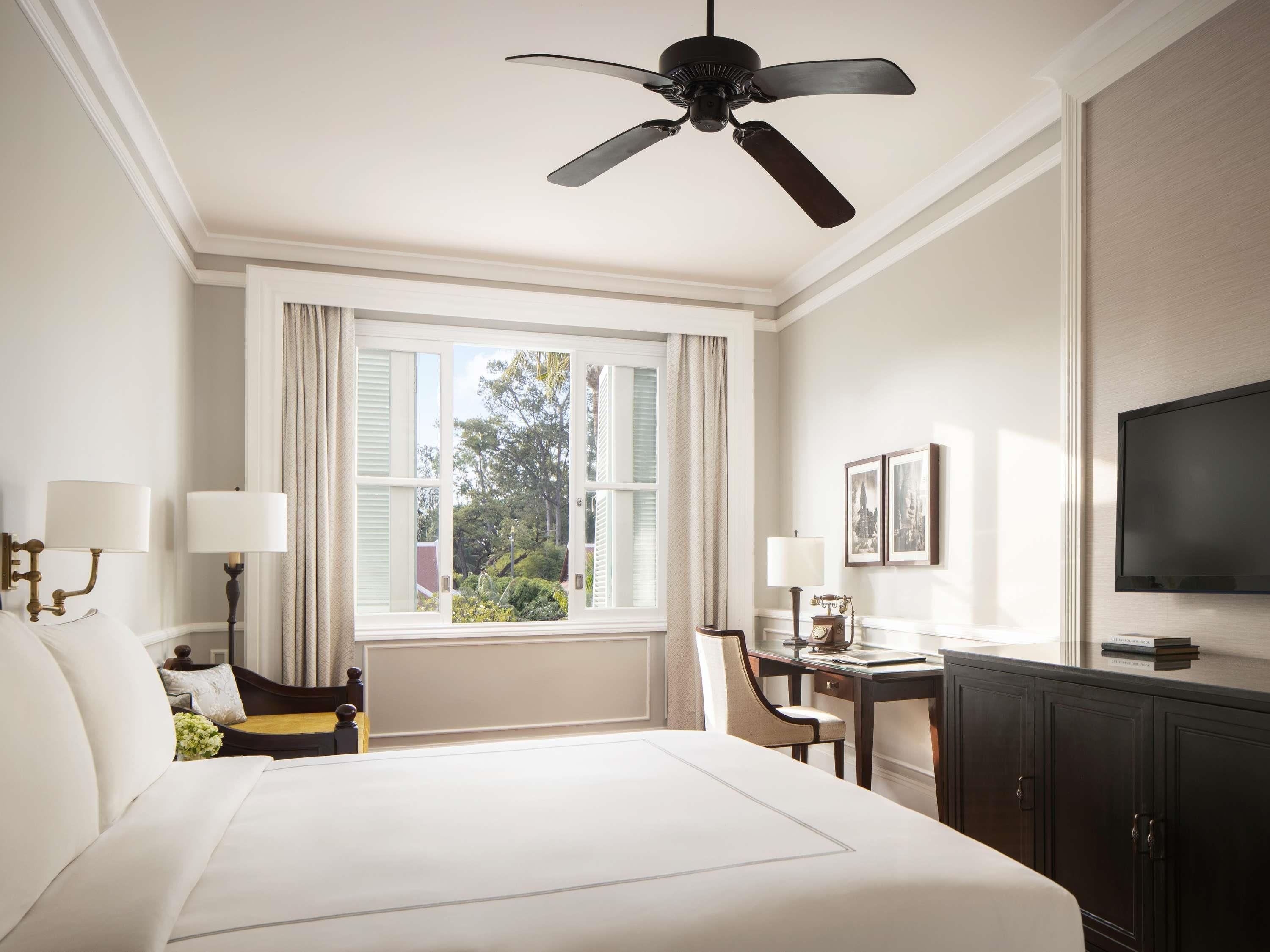 A hotel room with a bed, a desk, a chair, a television, and a ceiling fan.