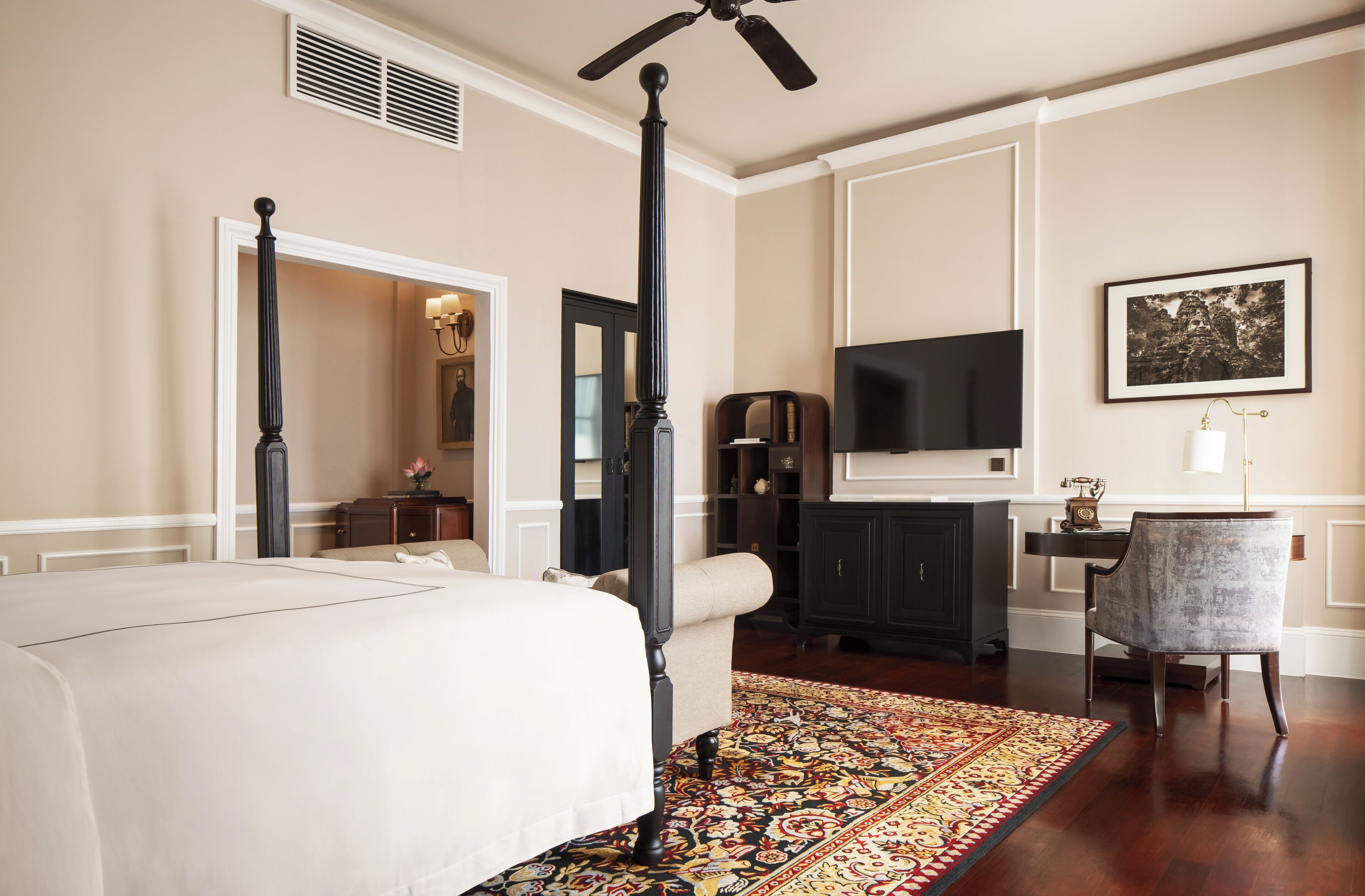 A bedroom with a four-poster bed, a television, a desk with a chair, and a patterned rug.