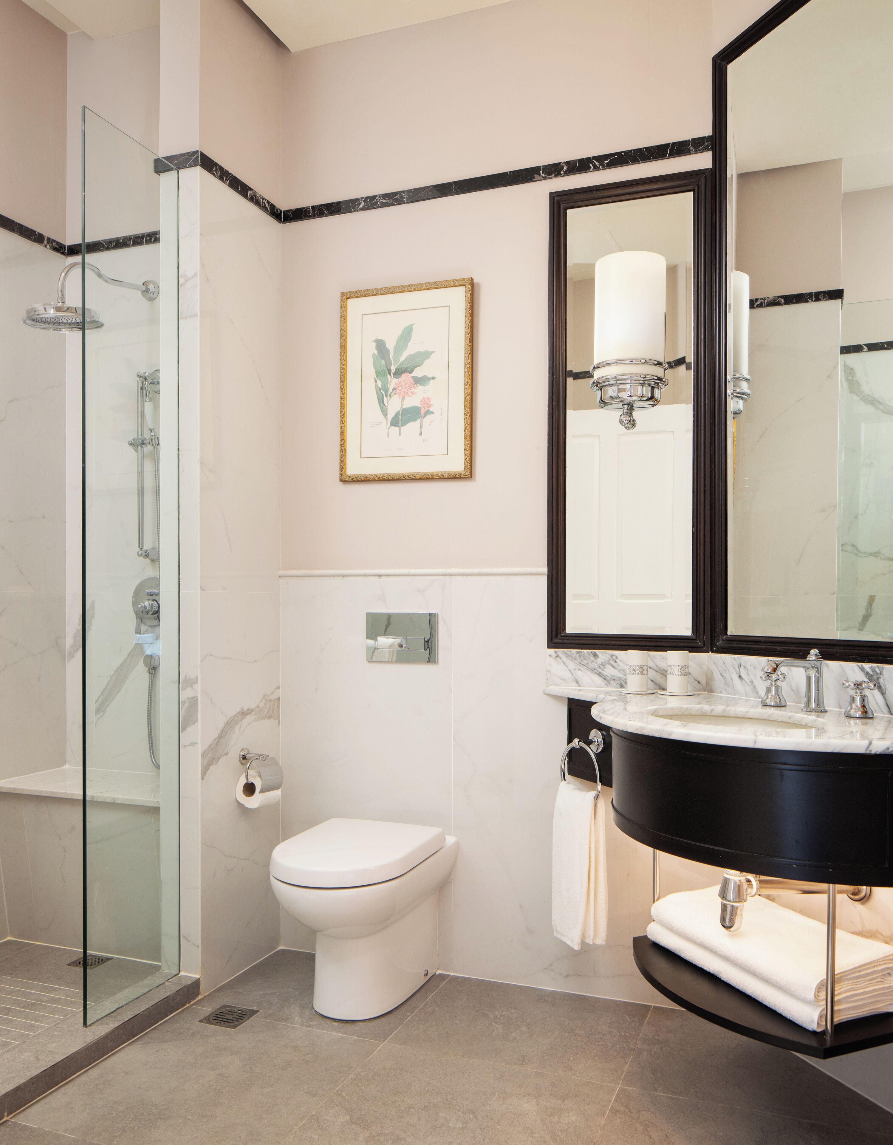 Un baño moderno con ducha de vidrio, inodoro blanco, lavabo negro con encimera de mármol y un espejo grande.