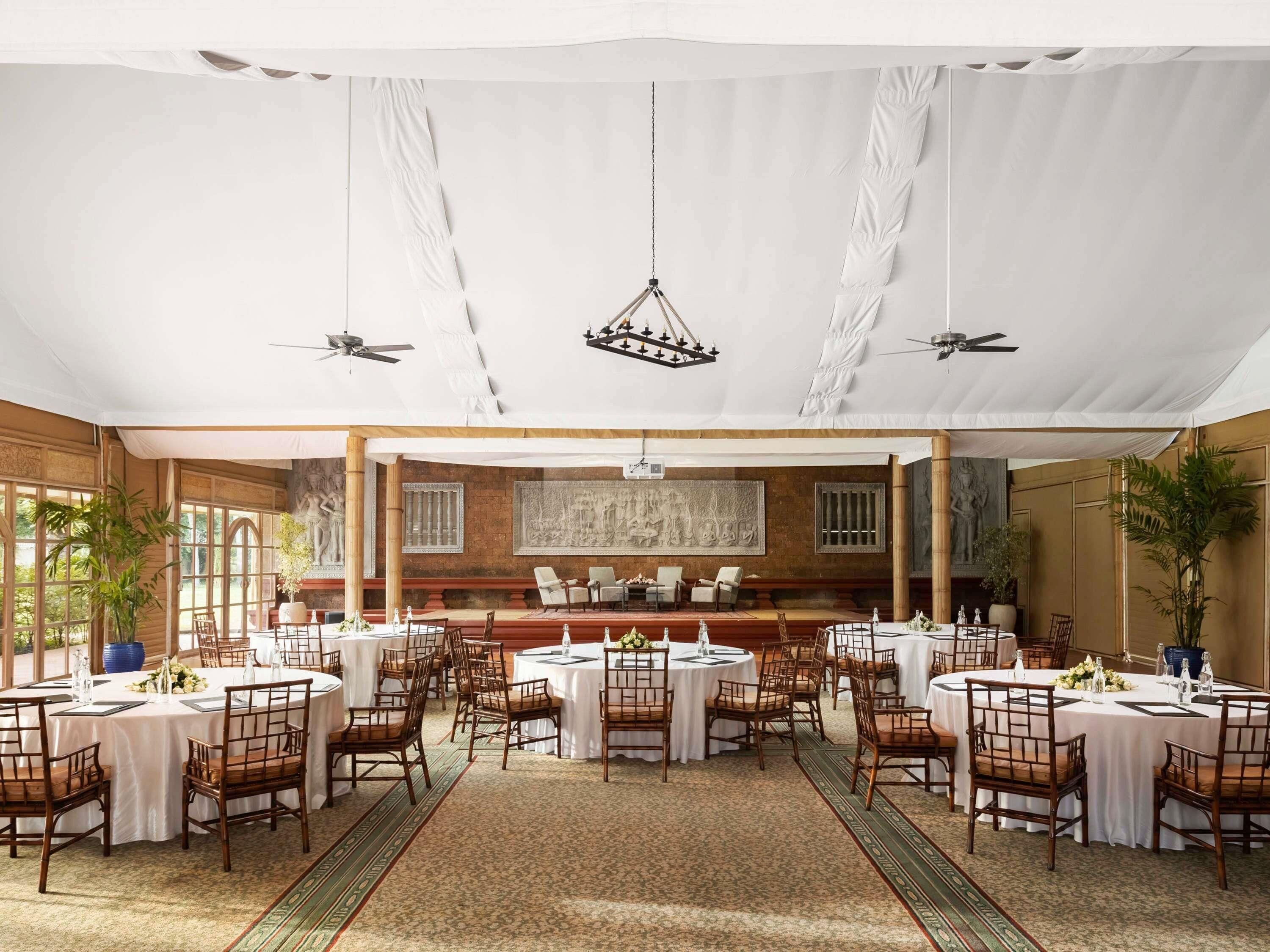 A spacious indoor dining area with round tables, wooden chairs, and a central stage.