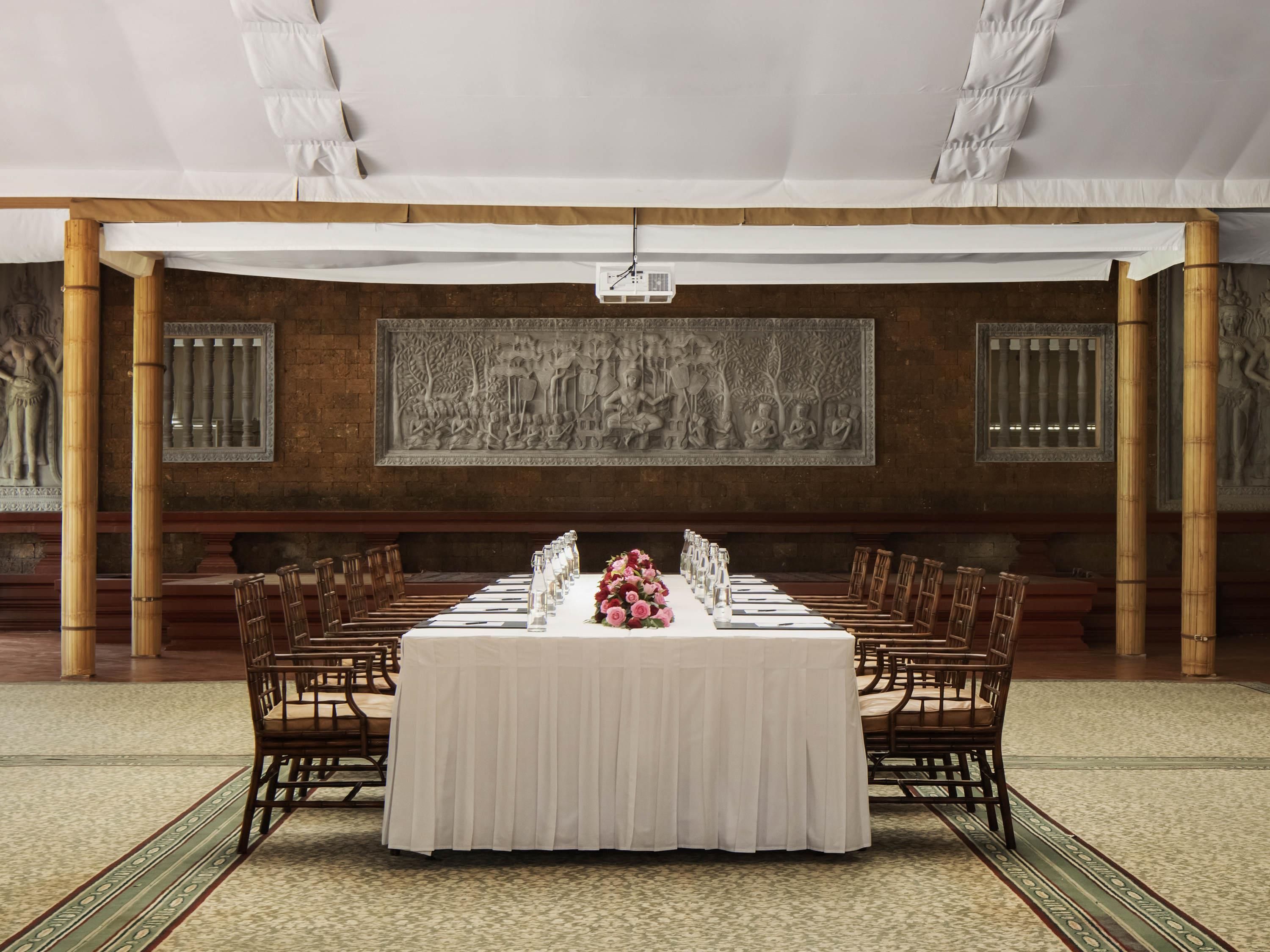 Un salón de banquetes con una larga mesa, sillas y una pared decorativa.