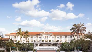 Un gran hotel con piscina, palmeras y un cielo azul despejado.