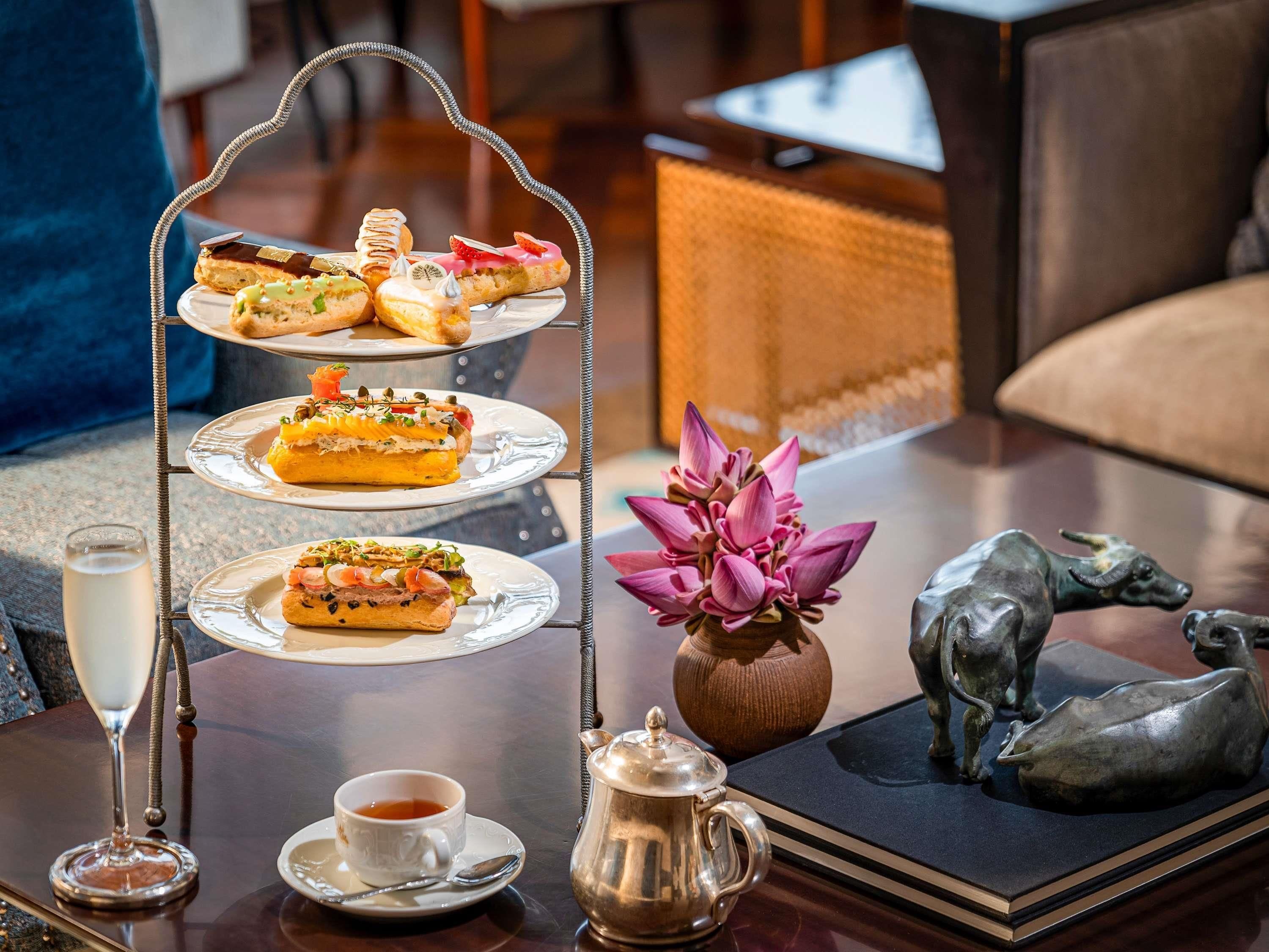 Ein gestaffeltes Desserttablett mit verschiedenen Backwaren, einer Teekanne, einer Tasse Tee und dekorativen Gegenständen auf einem Tisch.
