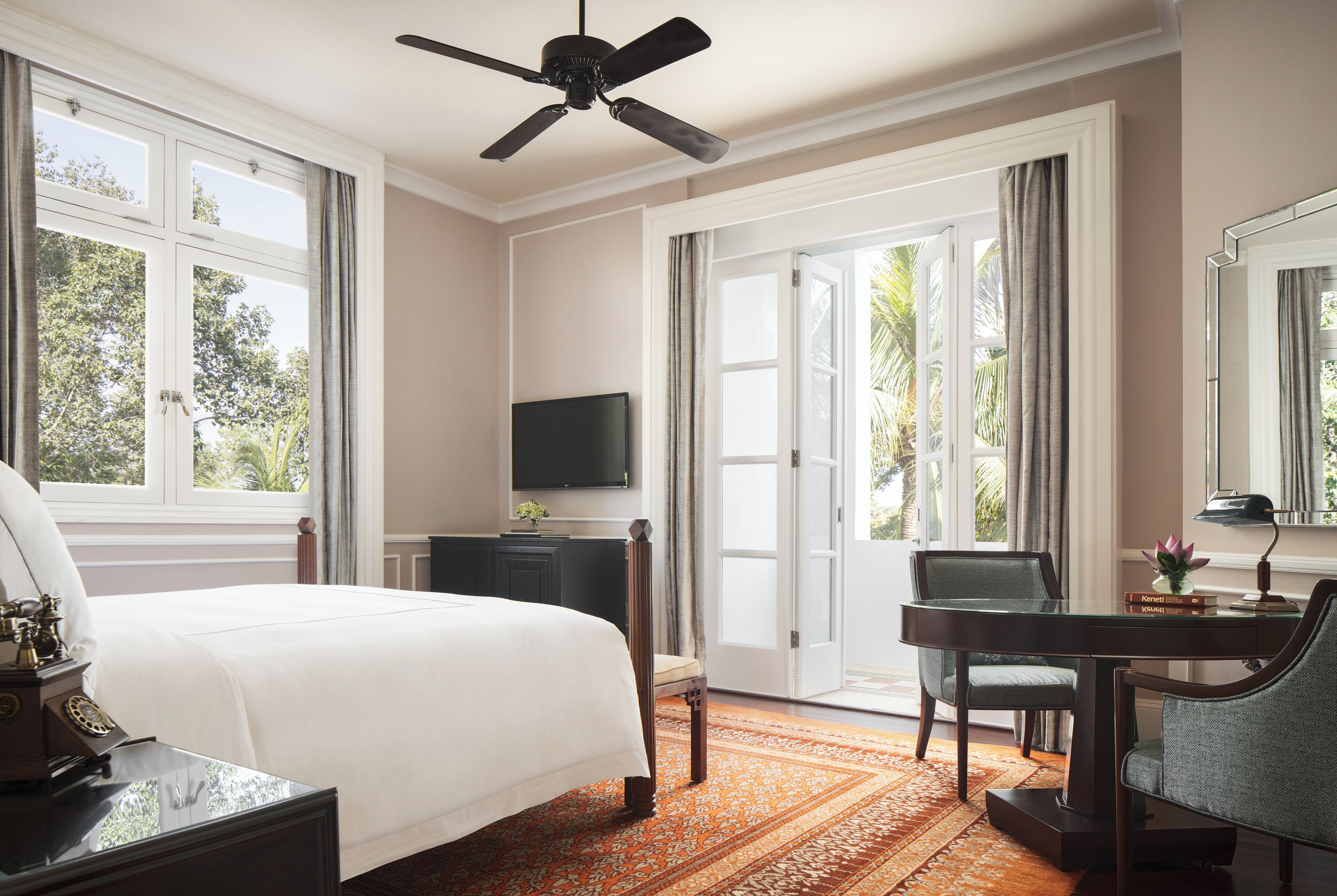 A hotel room with a bed, desk, chair, television, and large windows.