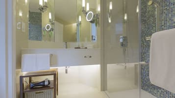 Ein modernes Badezimmer mit einer in Glas abgeschlossenen Dusche, einem Waschtisch mit Spiegel und einem Korbwäscher auf einem Regal.