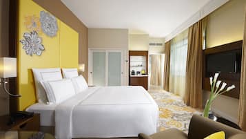 A hotel room with a large bed, a desk with a lamp, a TV, and a decorative wall piece.