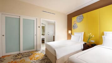 A hotel room with two beds, a bathroom visible through an open door, and a yellow accent wall with a floral design.