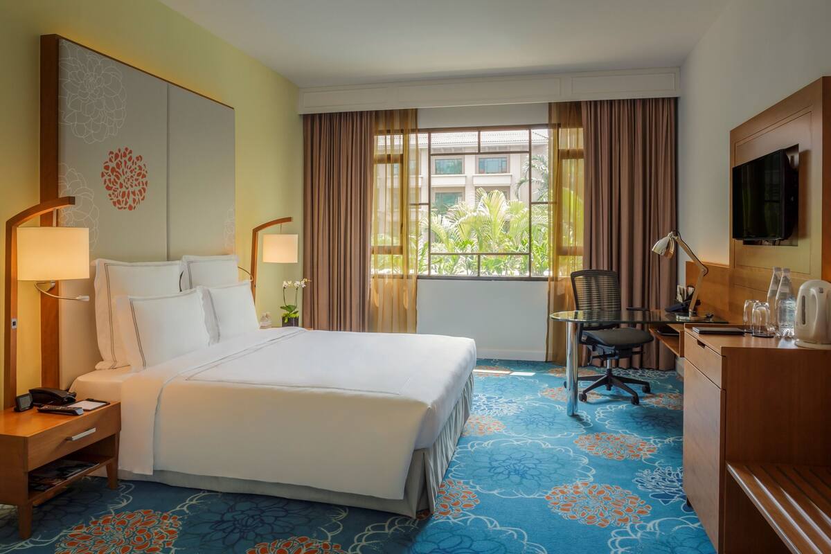 A hotel room with a large bed, a desk, a chair, a TV, and a window with curtains.