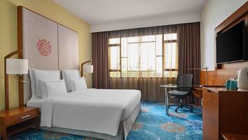 Una habitación de hotel con una cama grande, un escritorio con silla, un televisor y una ventana con cortinas.
