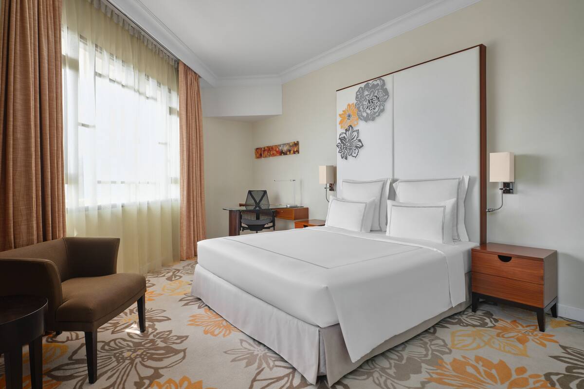 A hotel room with a large bed, a desk, a chair, and a nightstand.