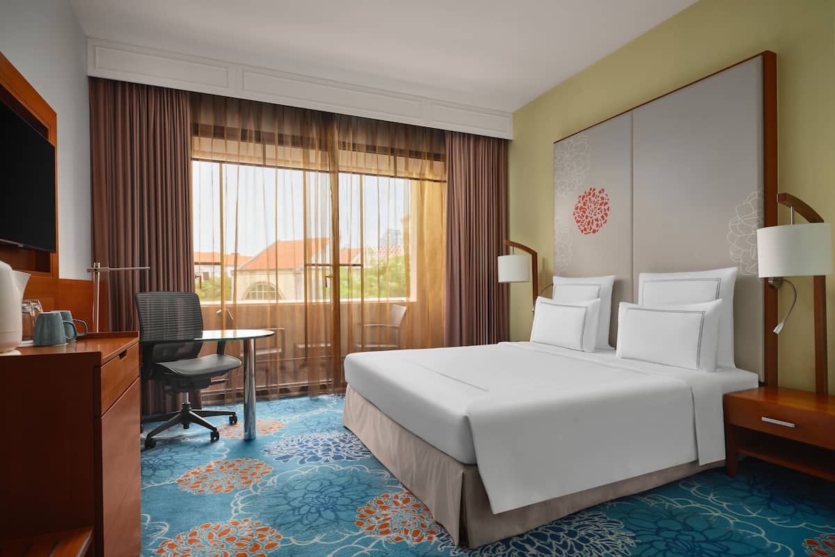 A hotel room with a large bed, a desk with a chair, a television, and a window with curtains.