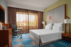 A hotel room with a large bed, a desk with a chair, a television, and a window with curtains.