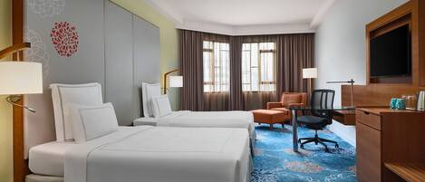 A hotel room with two beds, a desk, a chair, a TV, and a window with curtains.