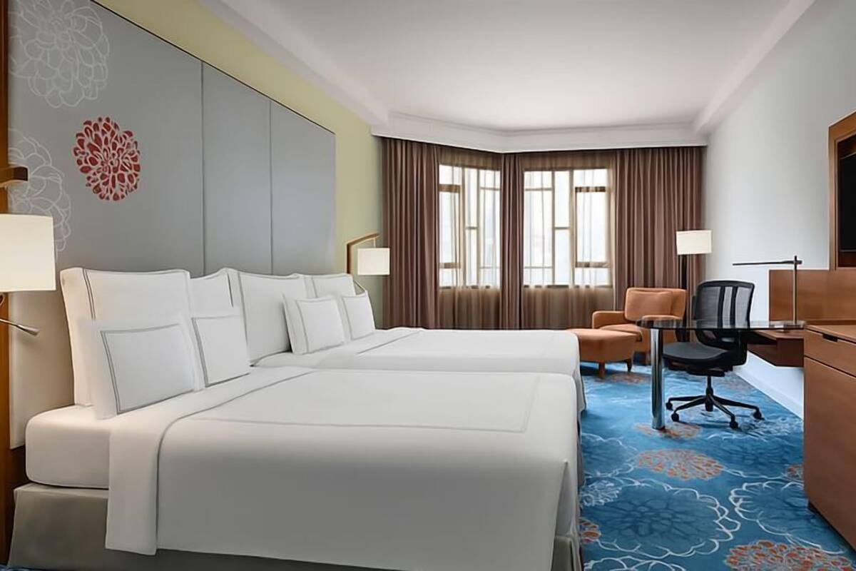 A hotel room with two beds, a desk, a chair, a TV, and a window with curtains.