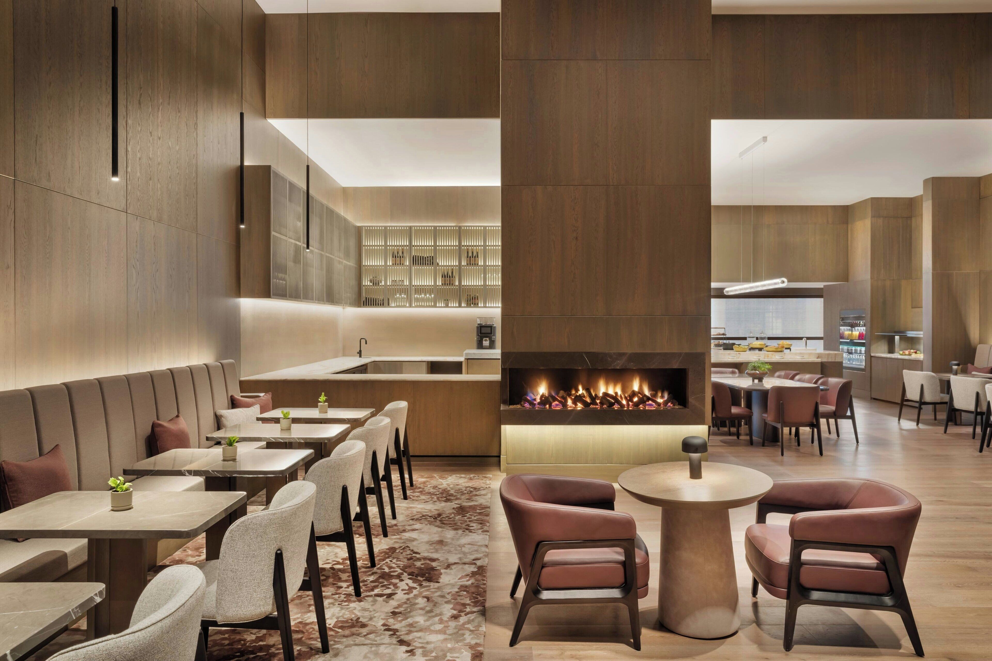 A modern interior with a central fireplace, seating areas, and a kitchen in the background.