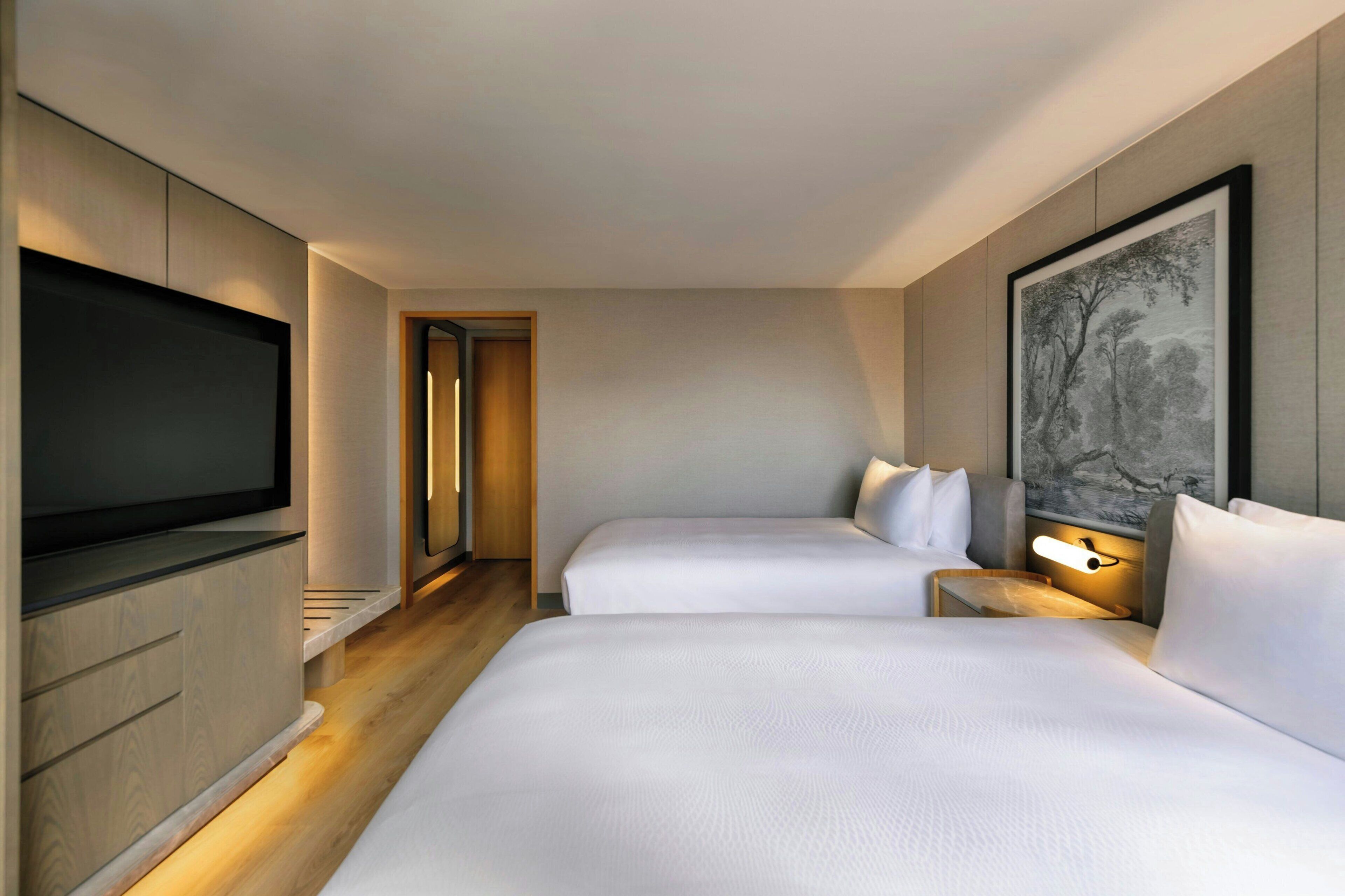 A hotel room with two beds, a flat-screen TV, a wooden cabinet, and a painting on the wall.