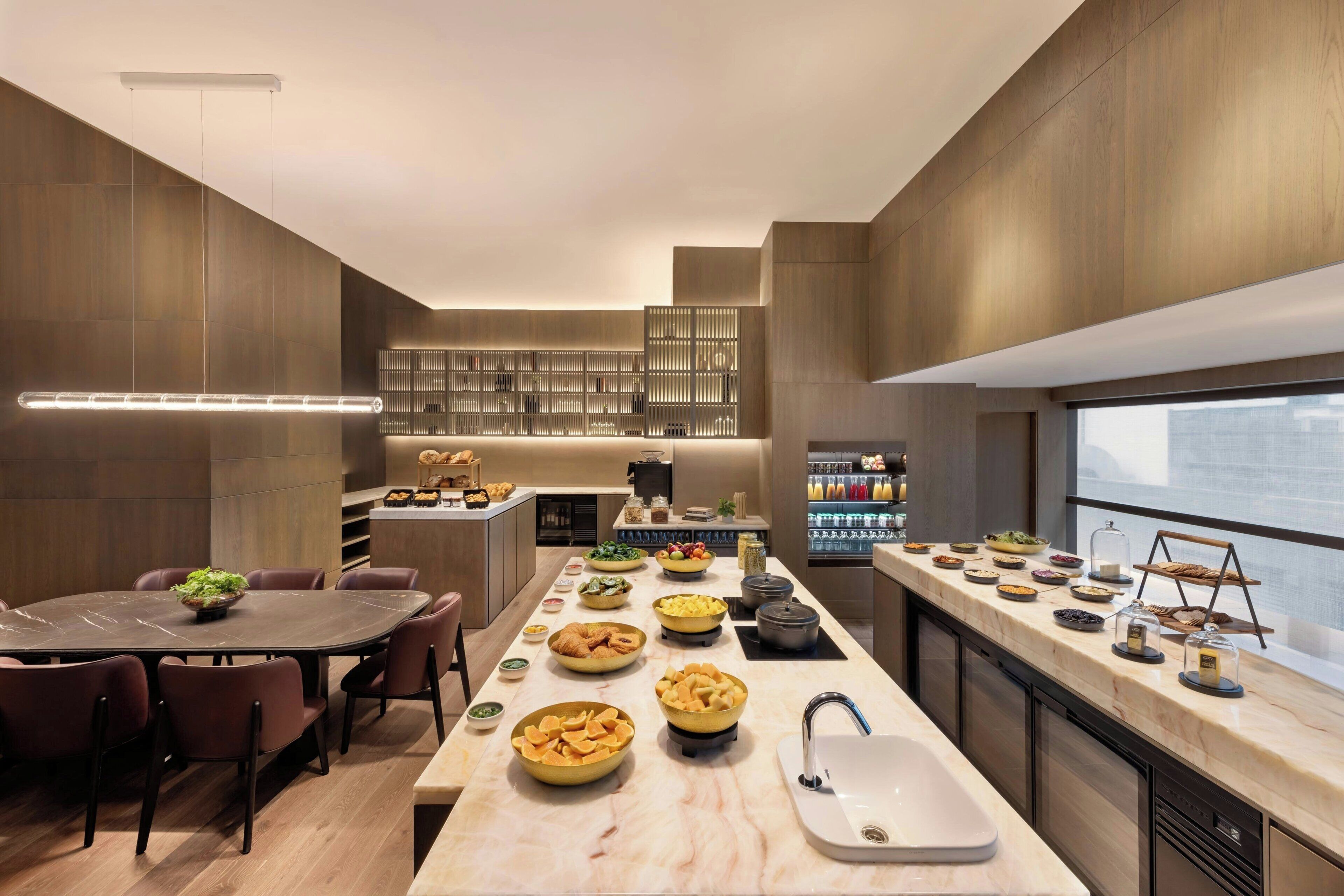 A modern kitchen with a marble countertop, a dining area with a large table, and a kitchen island with various food items.