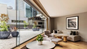 Un intérieur moderne avec un ensemble de canapés, une table ronde et des plantes en pot près d’une grande fenêtre donnant sur un paysage urbain.