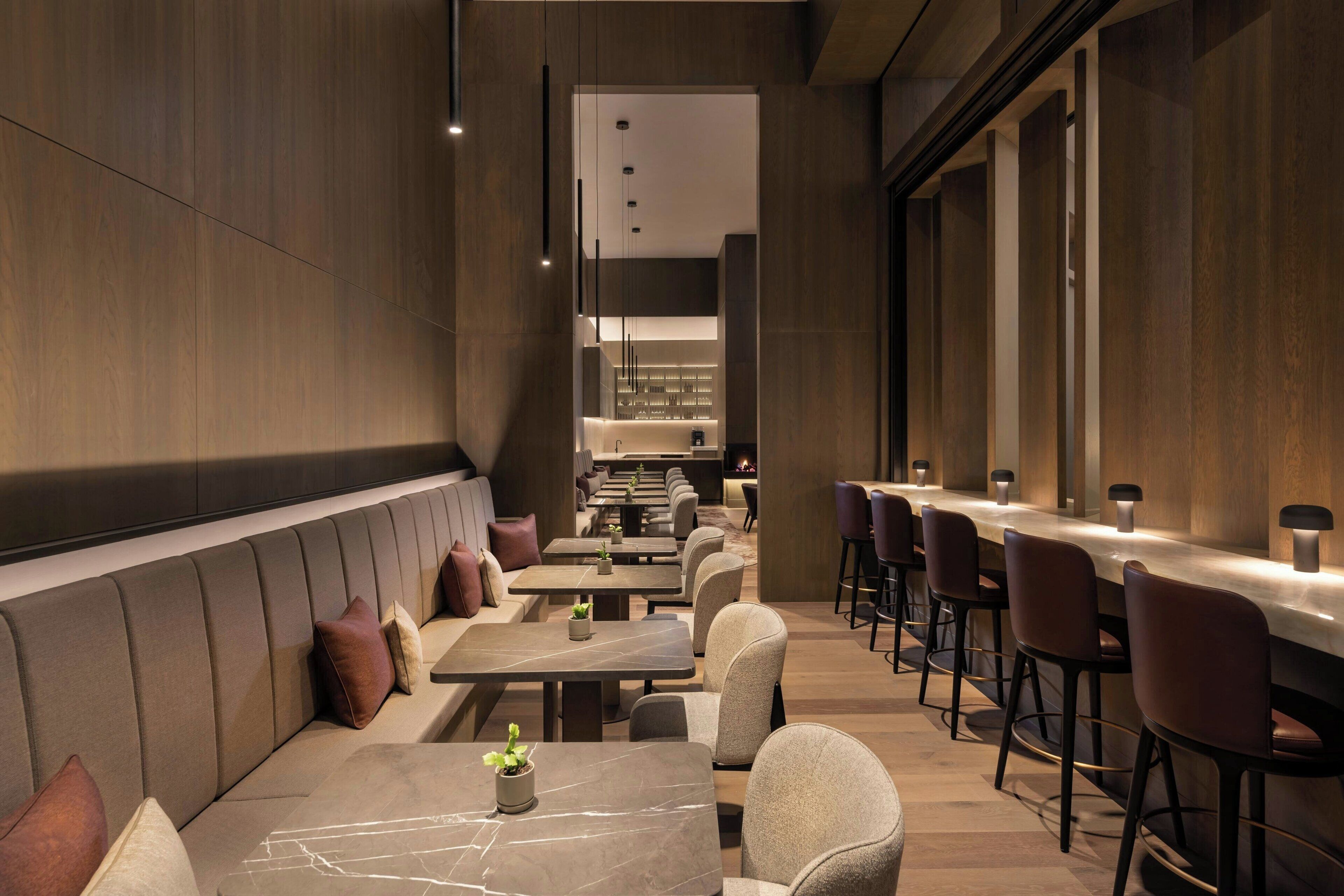 A modern restaurant with a long counter, cushioned seating, and pendant lighting.