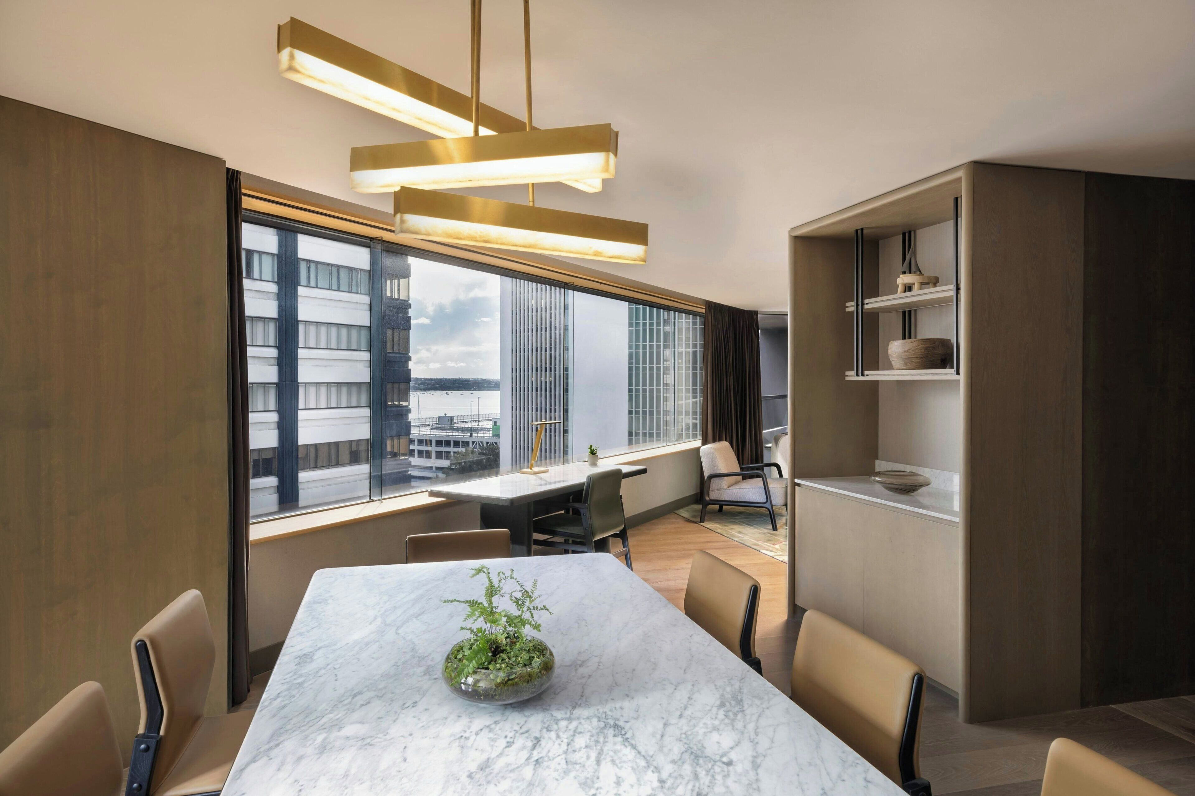 Een moderne eetruimte met een marmeren tafel, stoelen, een potplant en stadszicht door grote ramen.