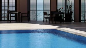 Una piscina con vistas al océano, un patio techado con mesas y sillas, y ventanas amplias.