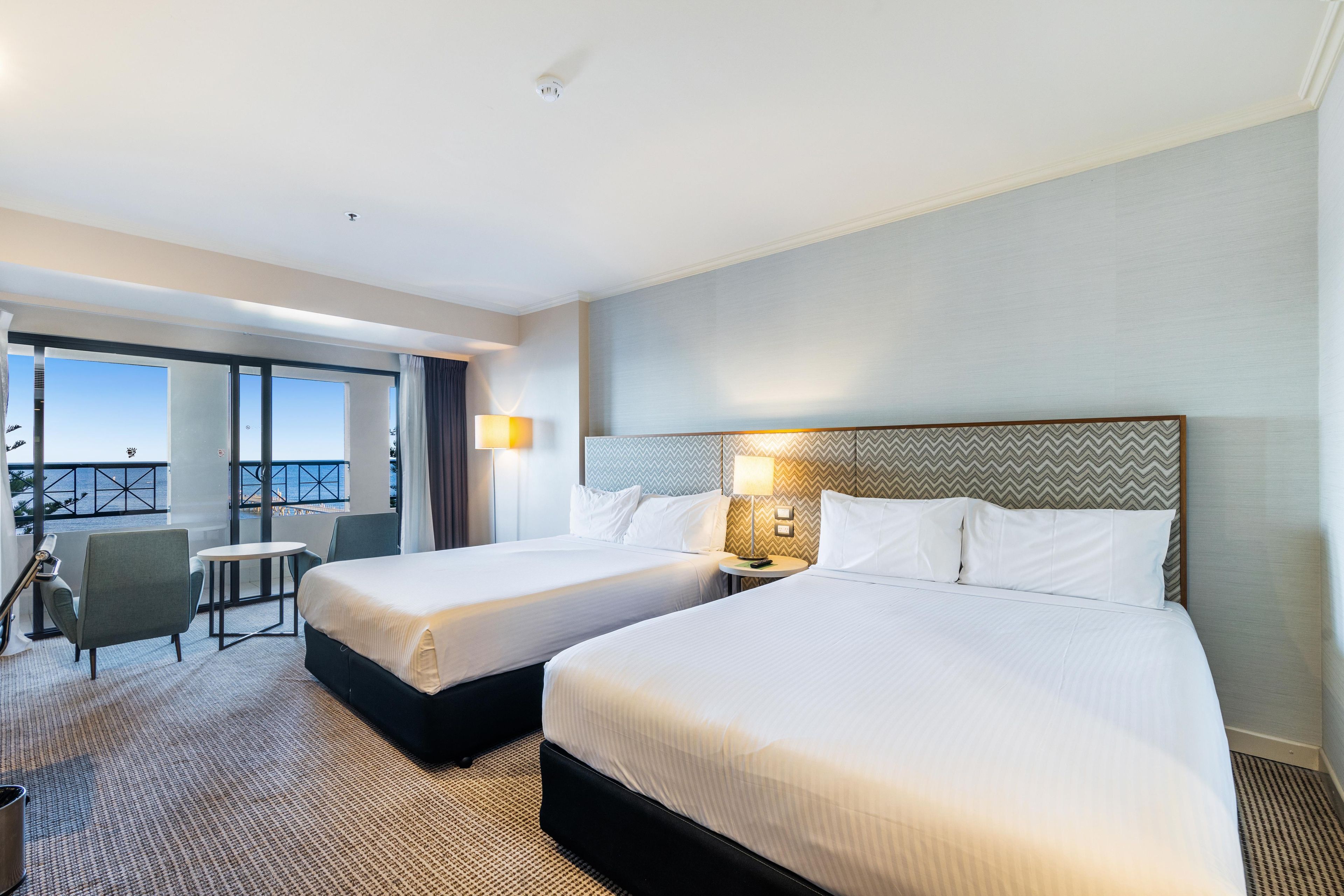 Une chambre d’hôtel avec deux lits, un balcon avec vue, un bureau et une chaise.
