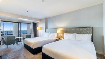 Habitación de hotel con dos camas, un balcón con vistas, un escritorio y una silla.
