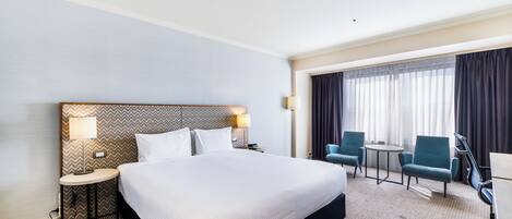Habitación de hotel con una cama grande, dos mesitas de noche con lámparas, un escritorio con silla y una pequeña mesa con dos sillas.