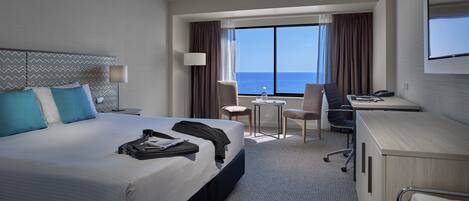 Habitación de hotel con cama, escritorio, silla y vista al océano.