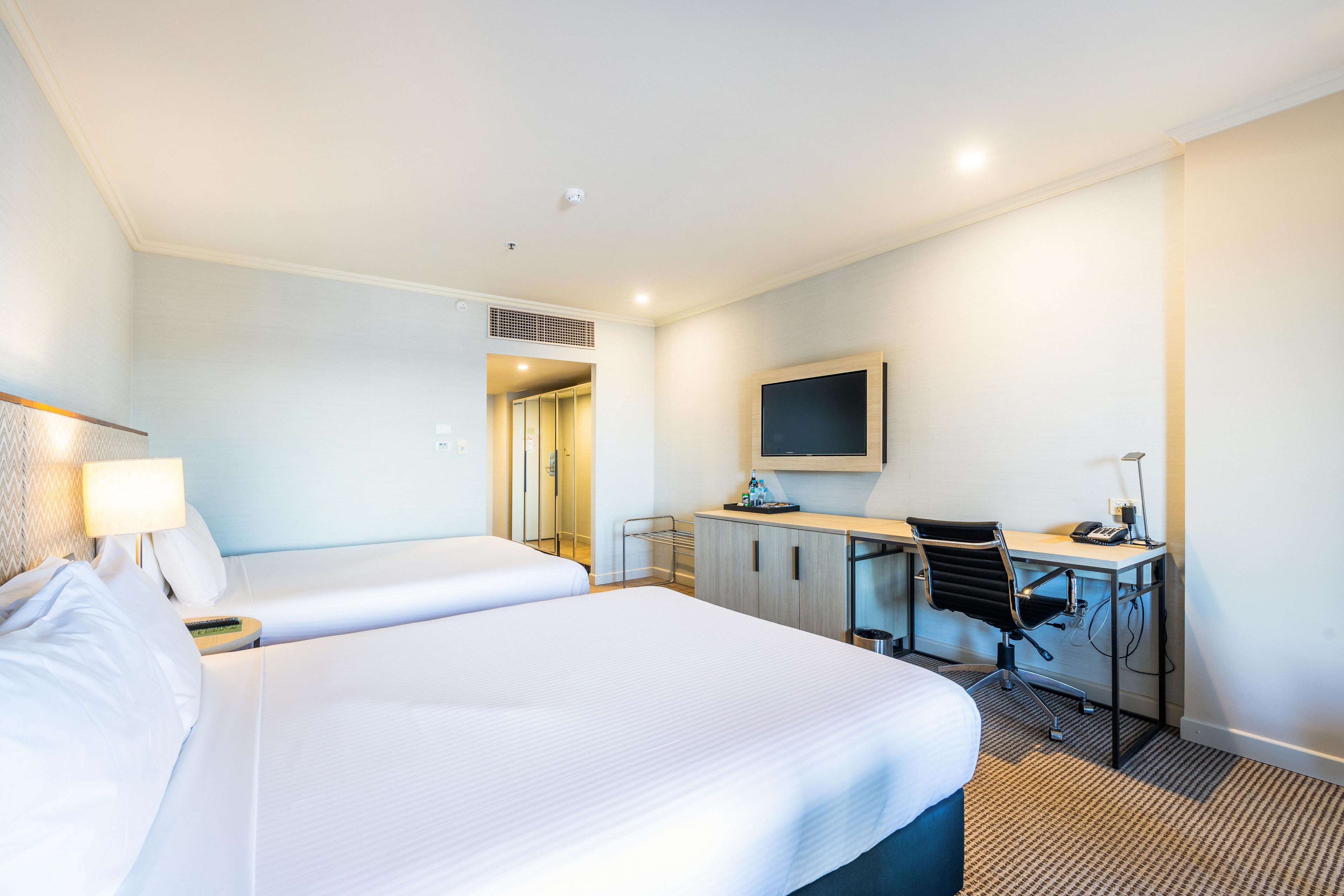 A hotel room with two beds, a desk with a chair, a television, and a minibar.