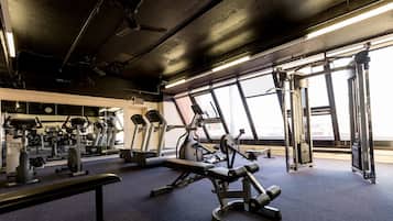 Un gimnasio con equipo de ejercicio diverso, ventanas amplias y un techo con vigas a la vista.