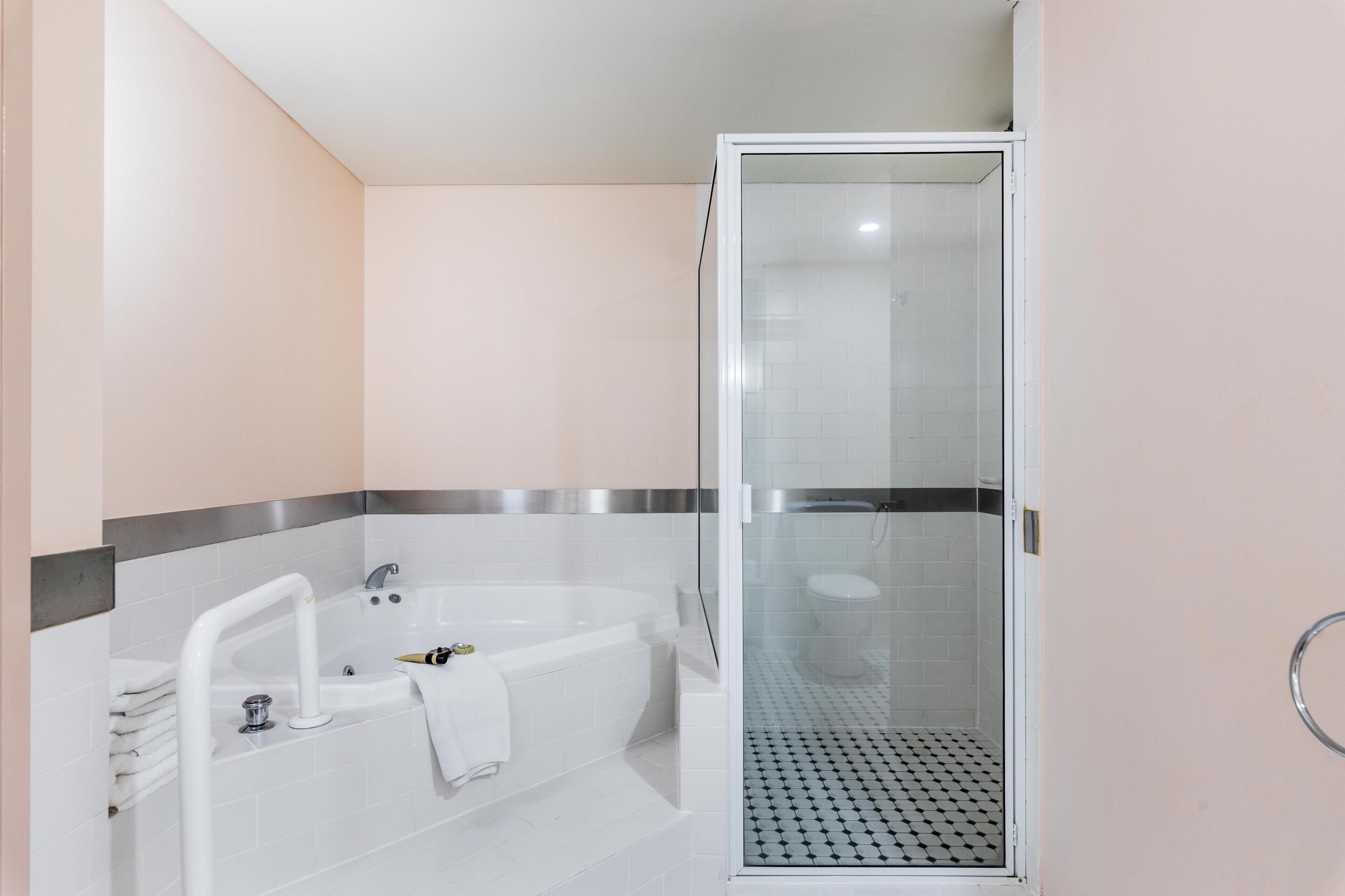 A modern bathroom with a glass-enclosed shower, a white bathtub with a handheld showerhead, and a towel rack.