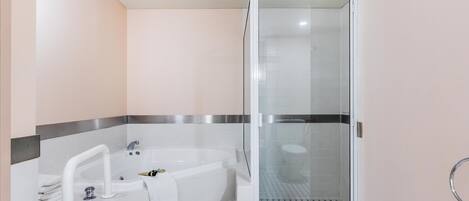 A modern bathroom with a glass-enclosed shower, a white bathtub with a handheld showerhead, and a towel rack.